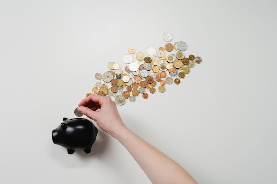 Person placing coin into a black piggy bank with scattered coins, symbolizing savings and finance